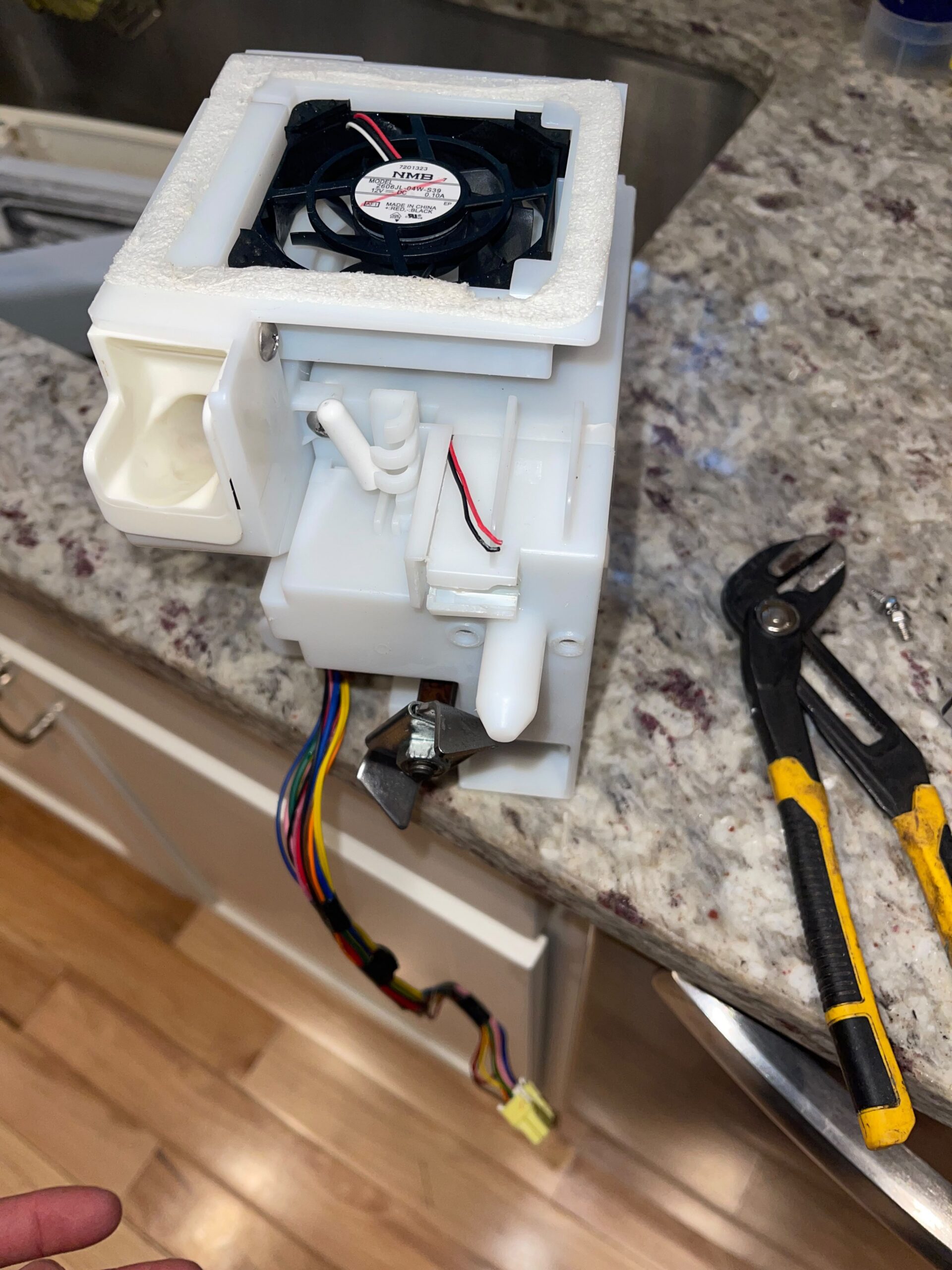 Appliance repair component with exposed wiring and cooling fan on a countertop